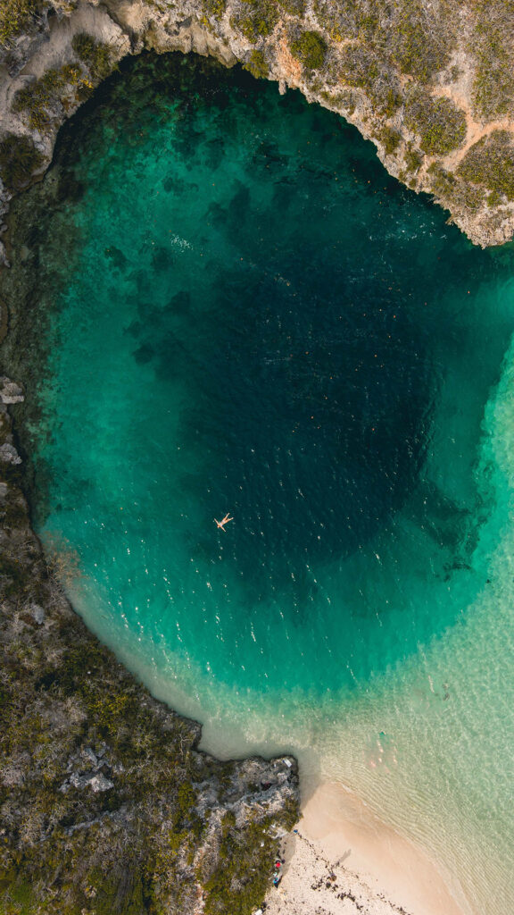 Aerial view of a person swimming in a deep blue lagoon at Caerula Mar Club, luxury resort on South Andros Island, Bahamas.